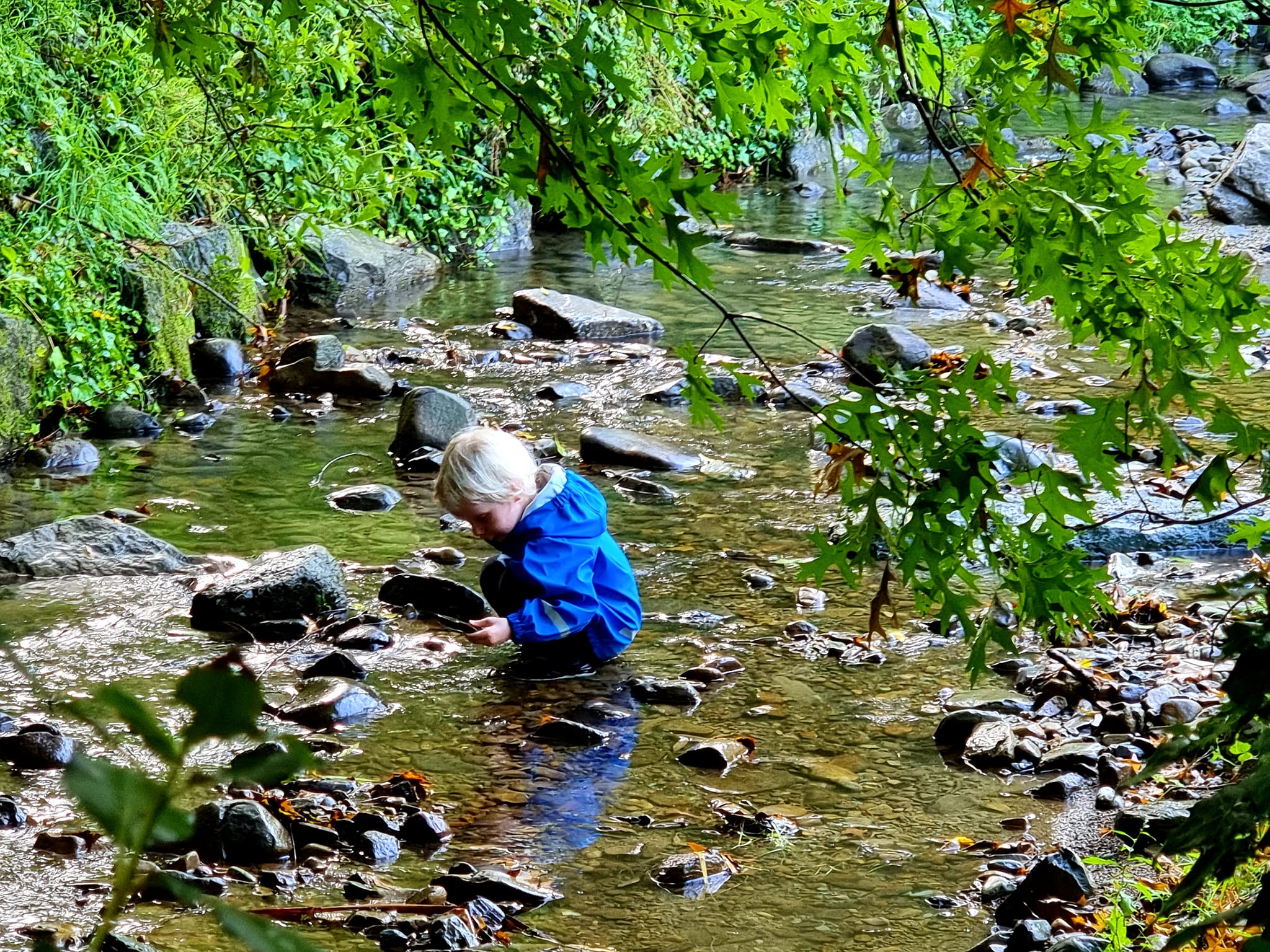 Outdoor play 2 Child in a blue coat squatting in a steam for outdoor play