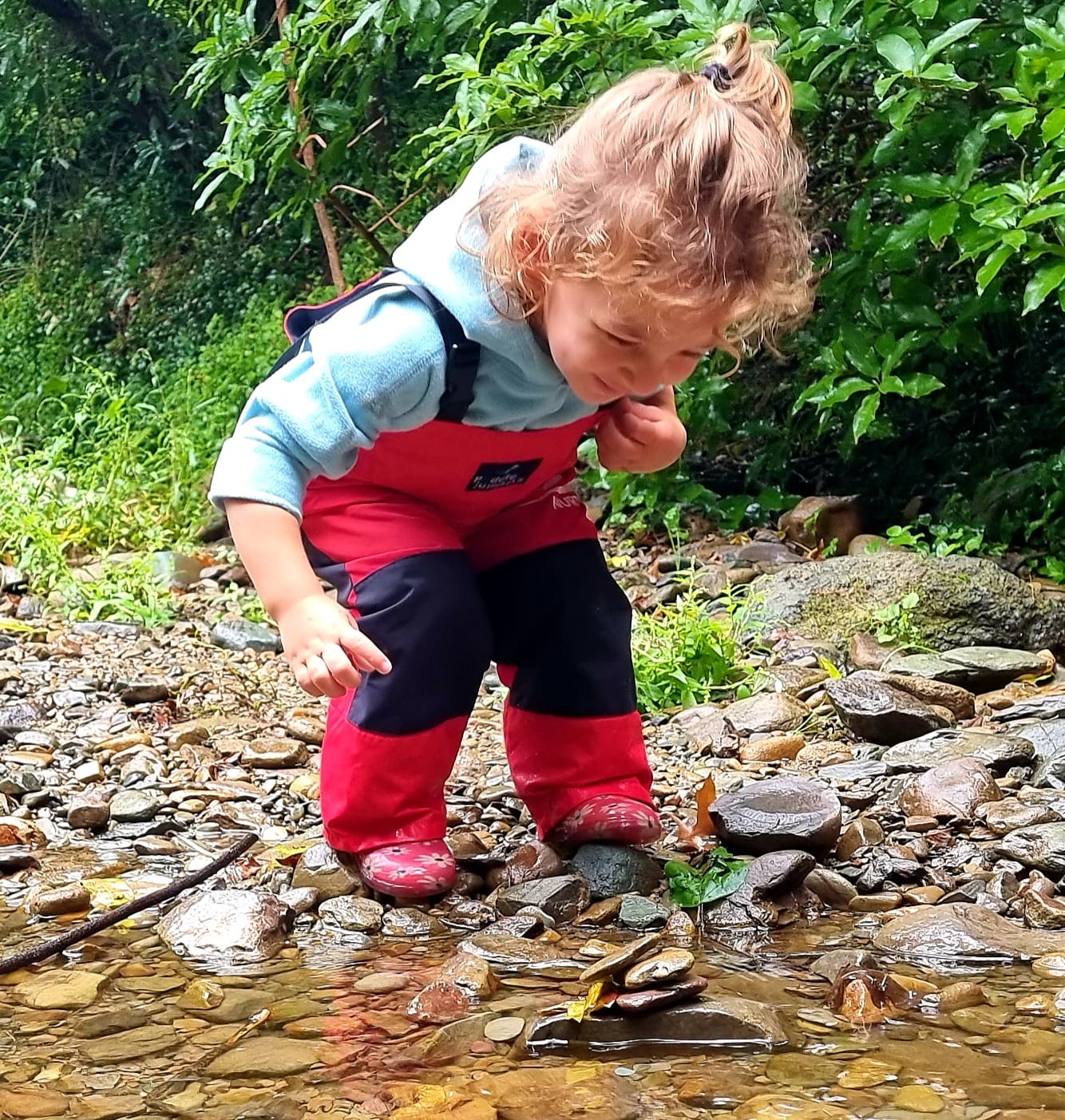 Outdoor play3 Child in red pants and gum boots stacking pebbles in a stream during outdoor play