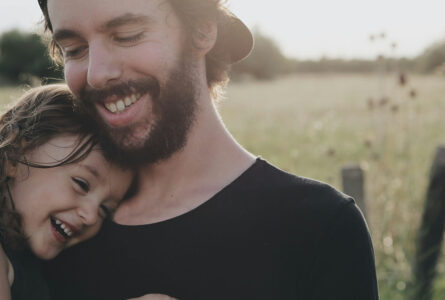 Young Dad Cuddling Child In Field