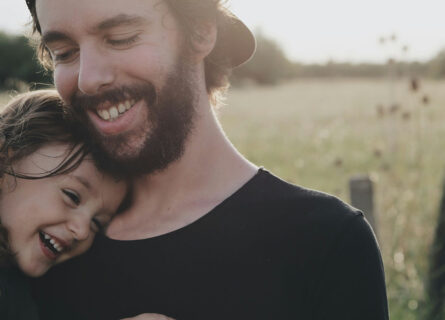 young dad cuddling child in field
